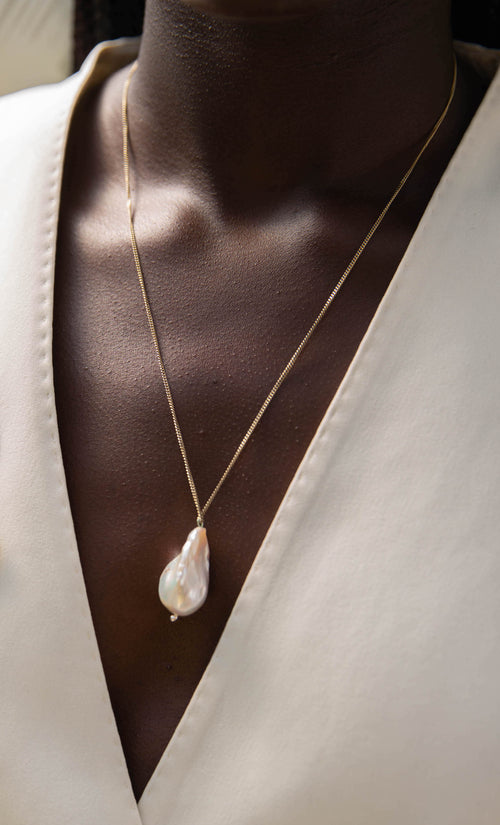 Model wearing handcrafted pearl necklace around neck, wearing a white blazer