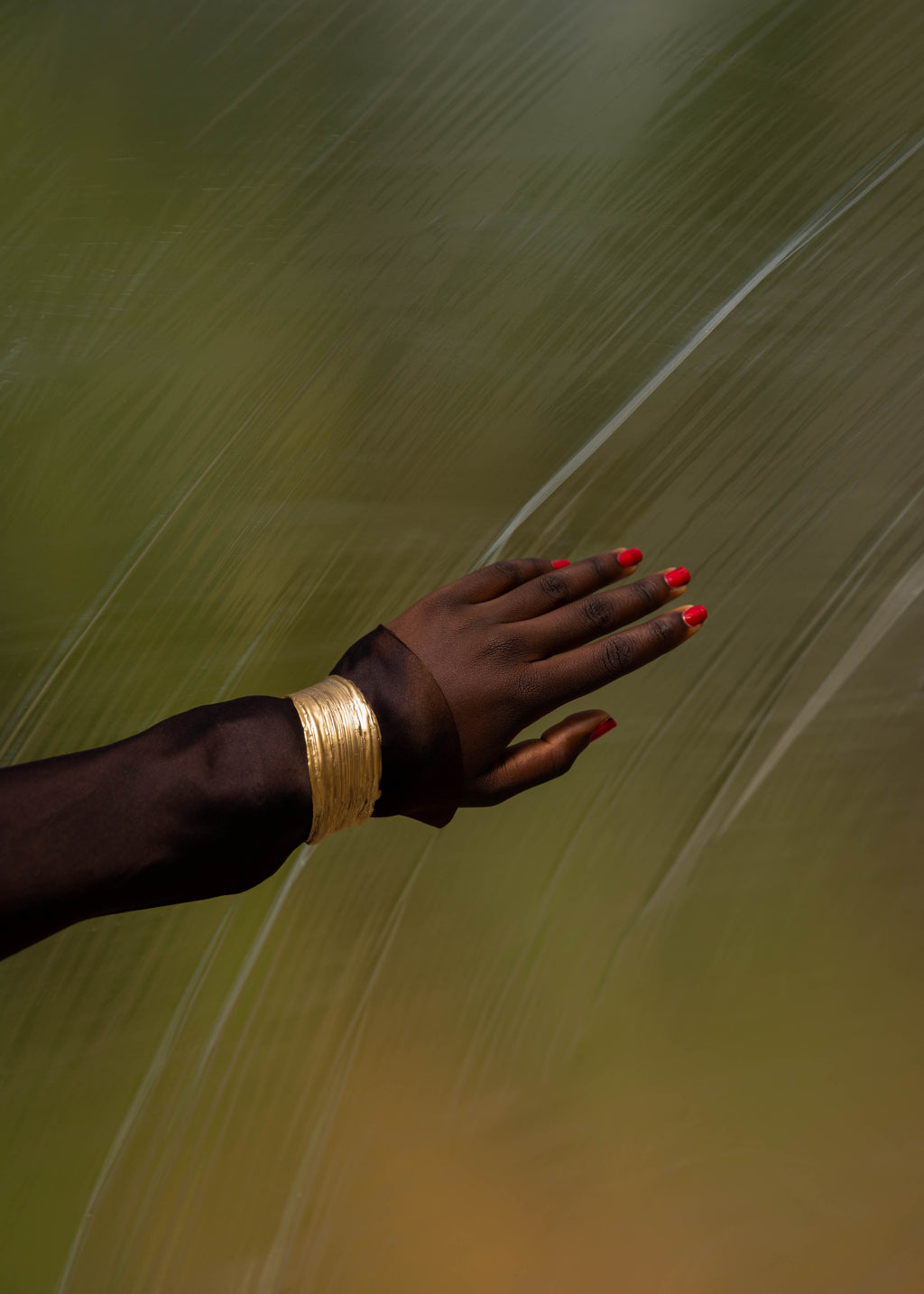 Hand with handcrafted gold bracelet and red nail polish against a blurred natural background