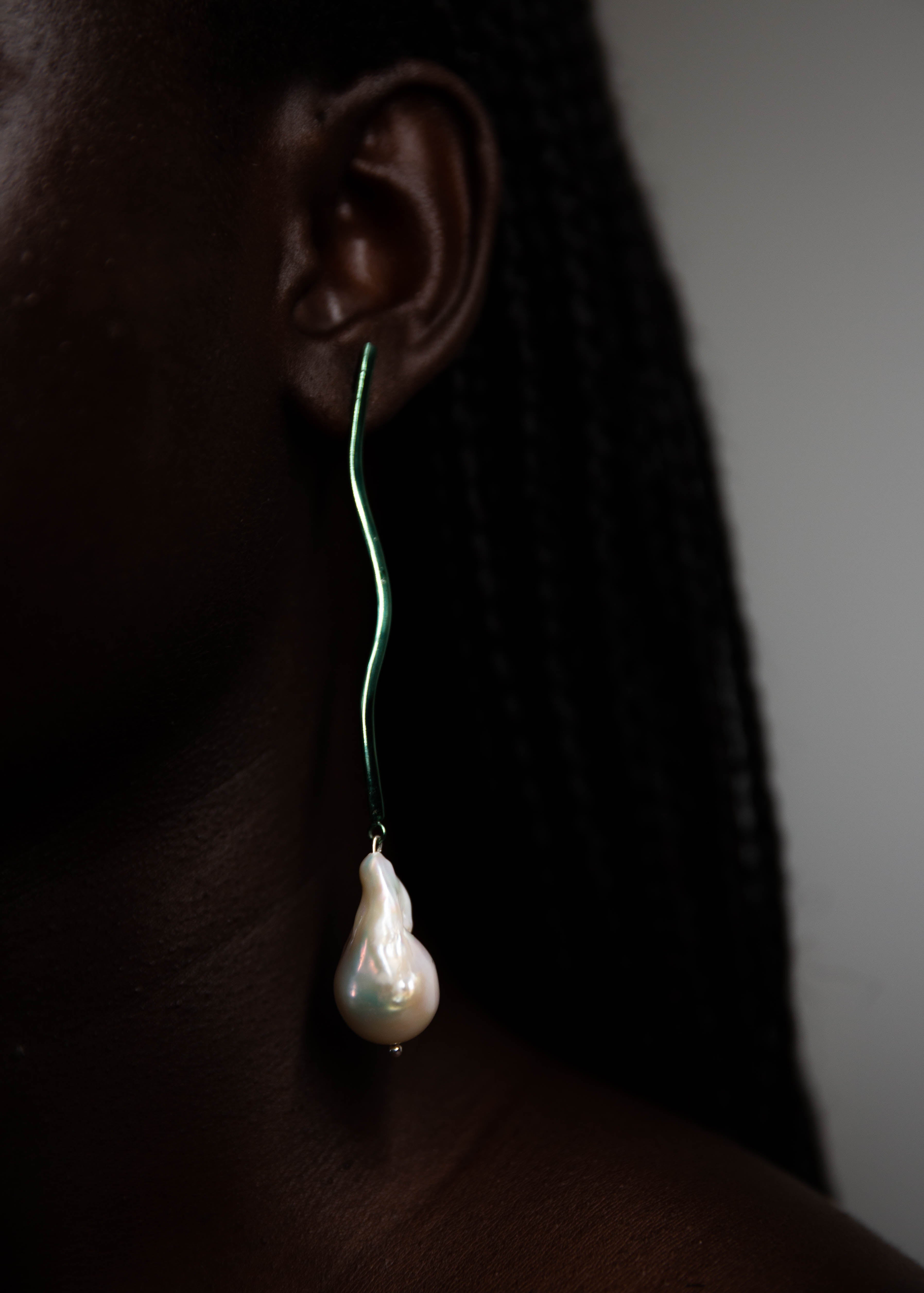 Handcrafted pearl earring with green stem worn on the ear, showing the side profile