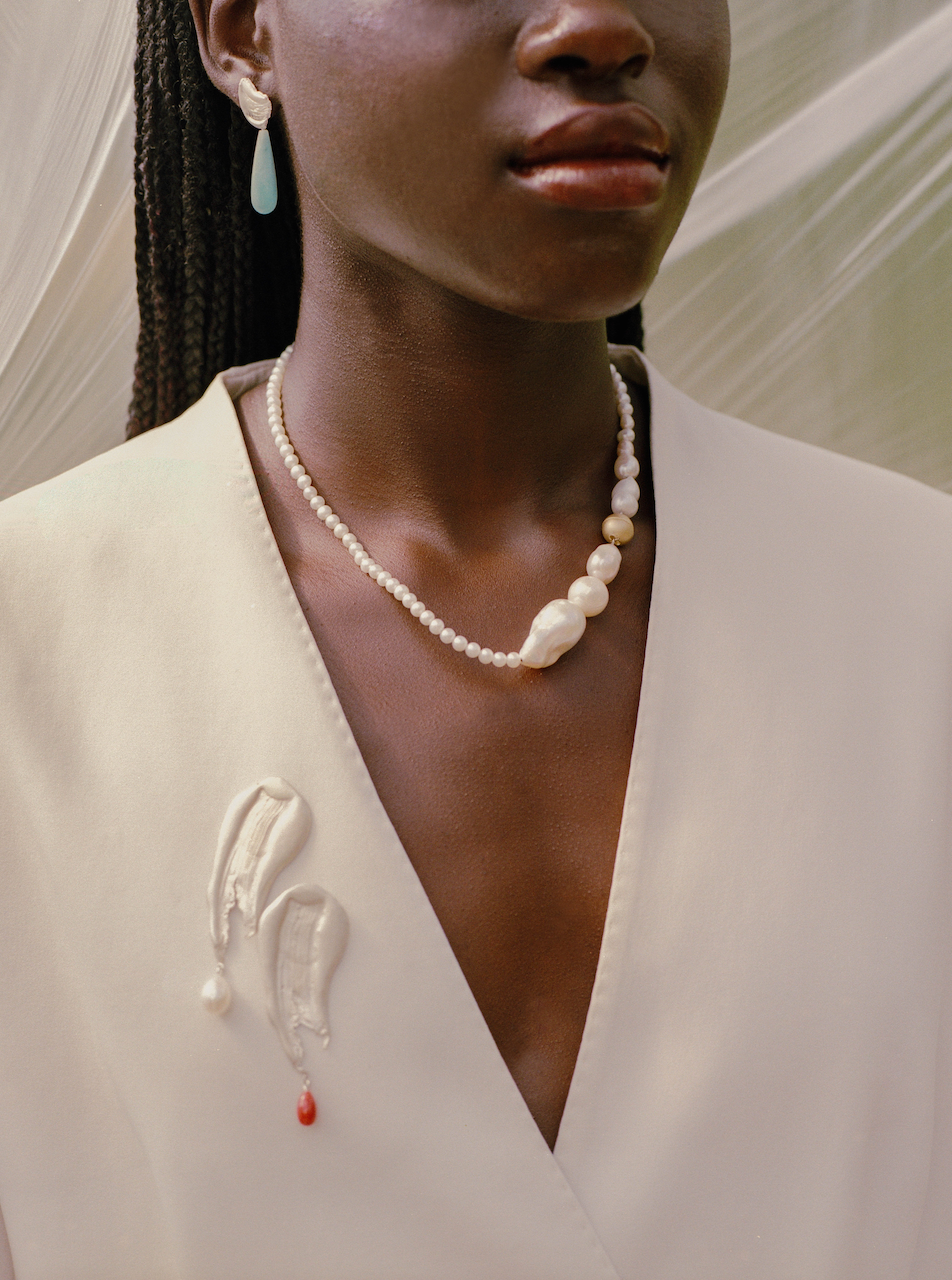 Woman wearing a handcrafted pearl necklace and two silver brooches with pearl pendants and red gemstone perndant with a neutral background