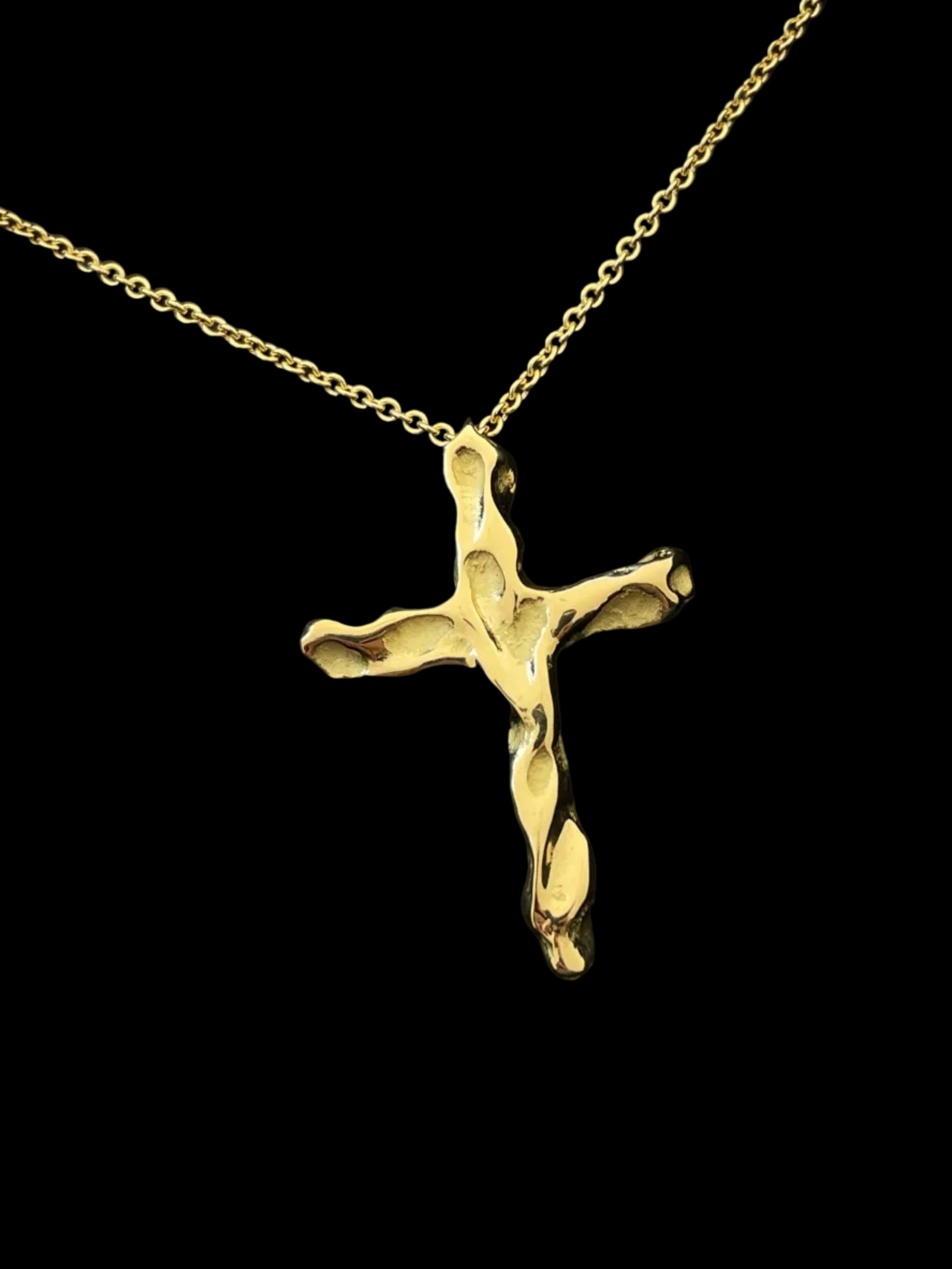 Handcrfated Gold cross pendant on a chain against a black background