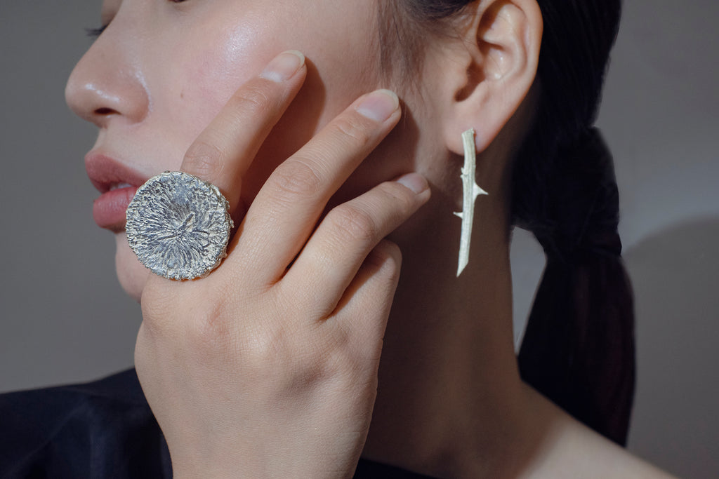 Close-up of a model wearing a handcrafted silver helios ring and touching their face with their hand.