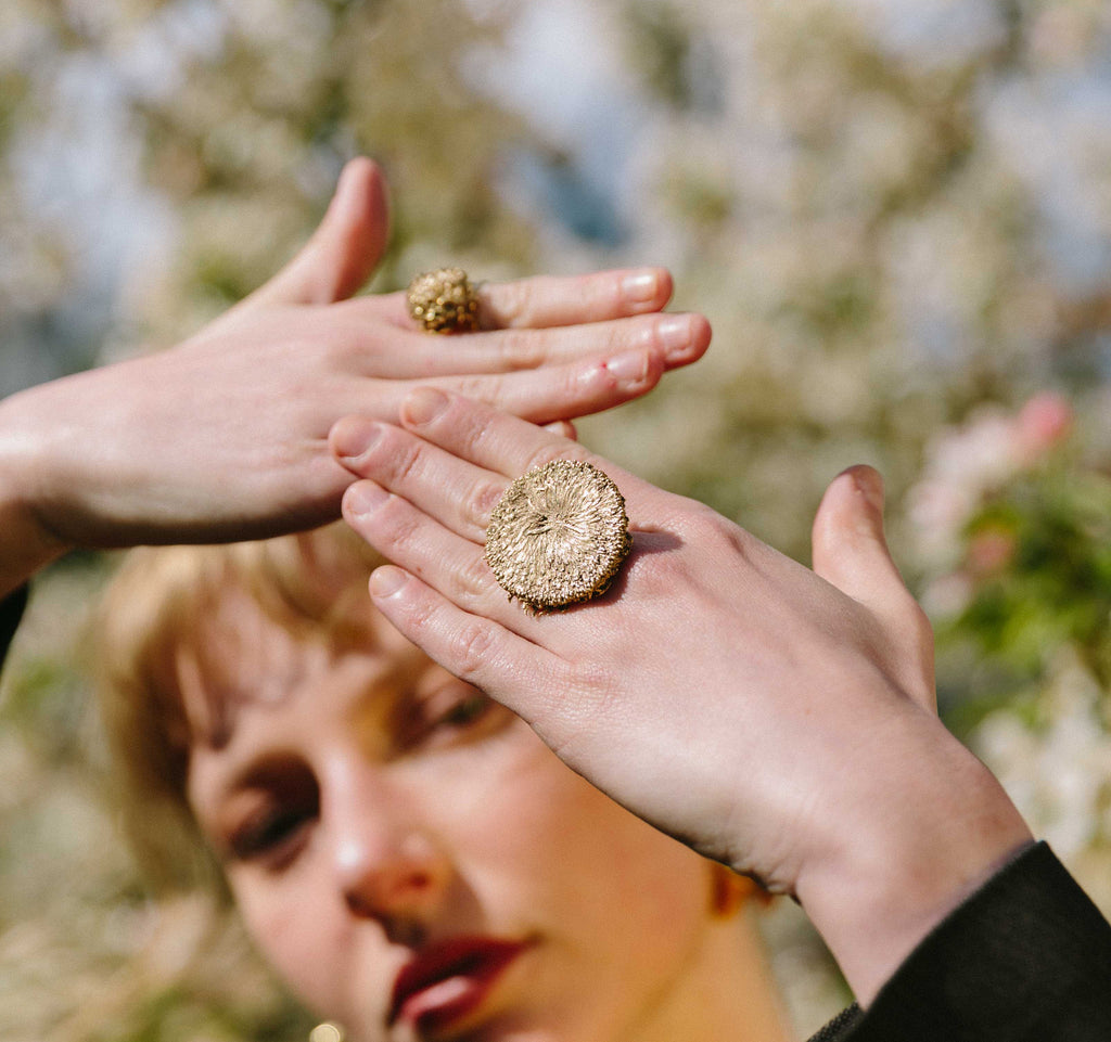 Model wearing a handcrafted gold helios ring in front of a blurred natural background