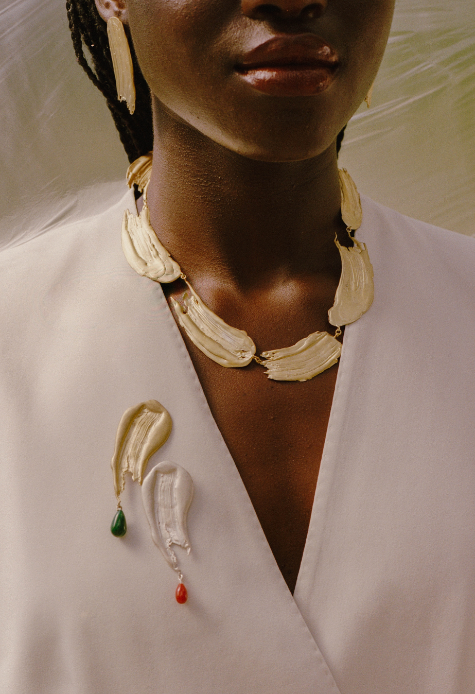 Handcrafted gold necklace, ade out of mutiple paint strokes, accompanied by two brooches. One silver and one gold with each a different gemstone. The gold with a green gemstone, the silver with a red gemstone