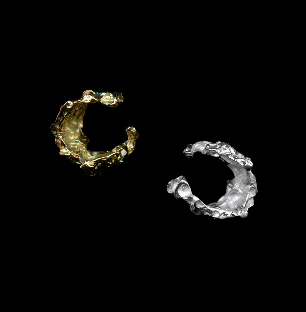 Two handcrafted bellis rings, one gold the other silver on black background