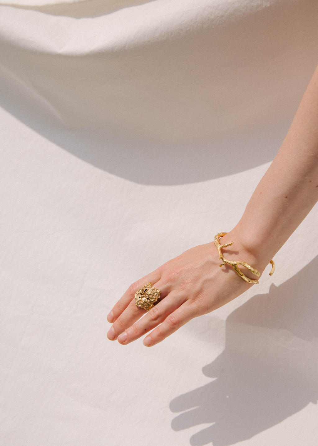 Hand wearing a handcrafted gold ring and bracelet on a light background