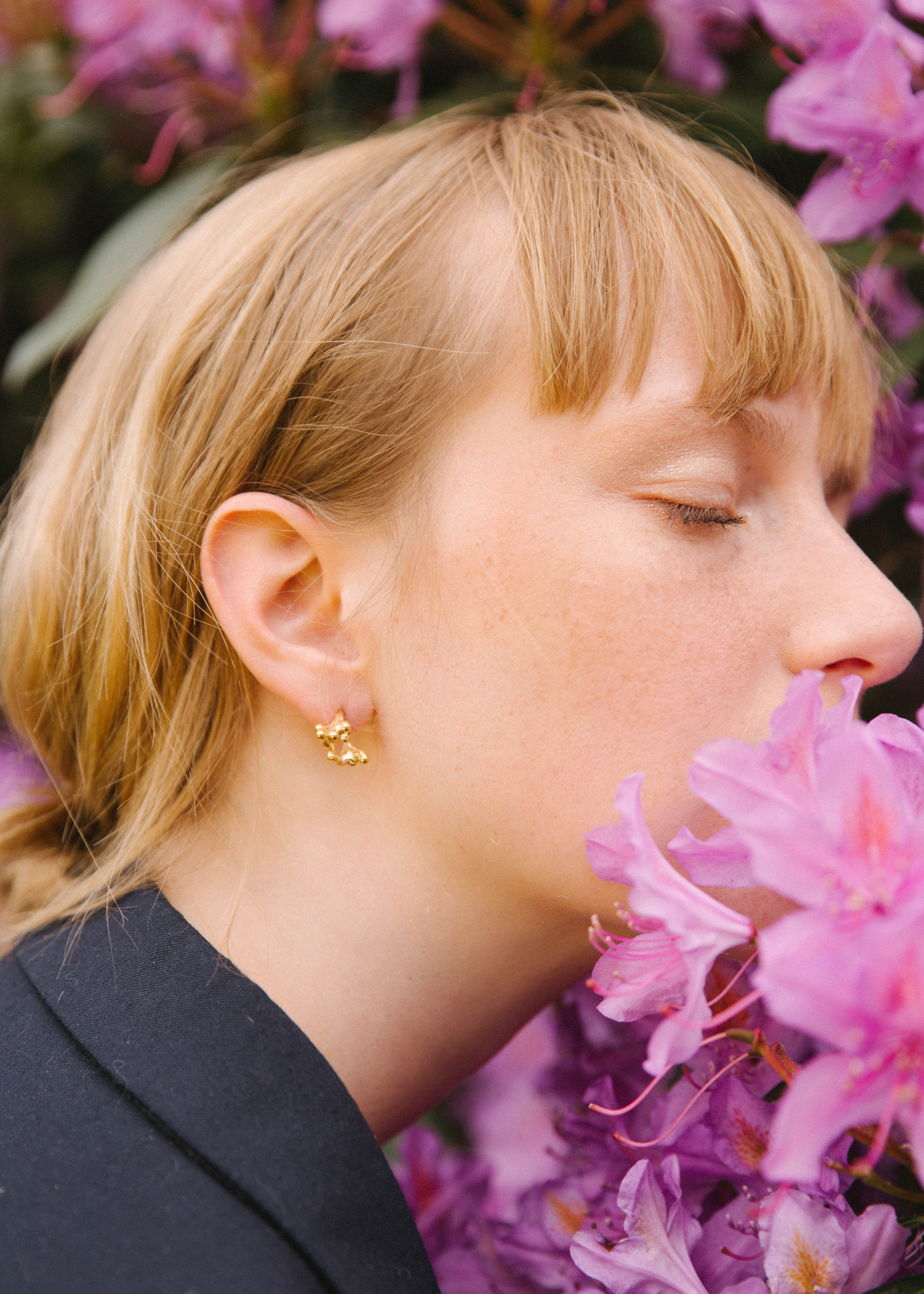 handcrfated gold rubella earrings worn by model who is smelling a purple flower