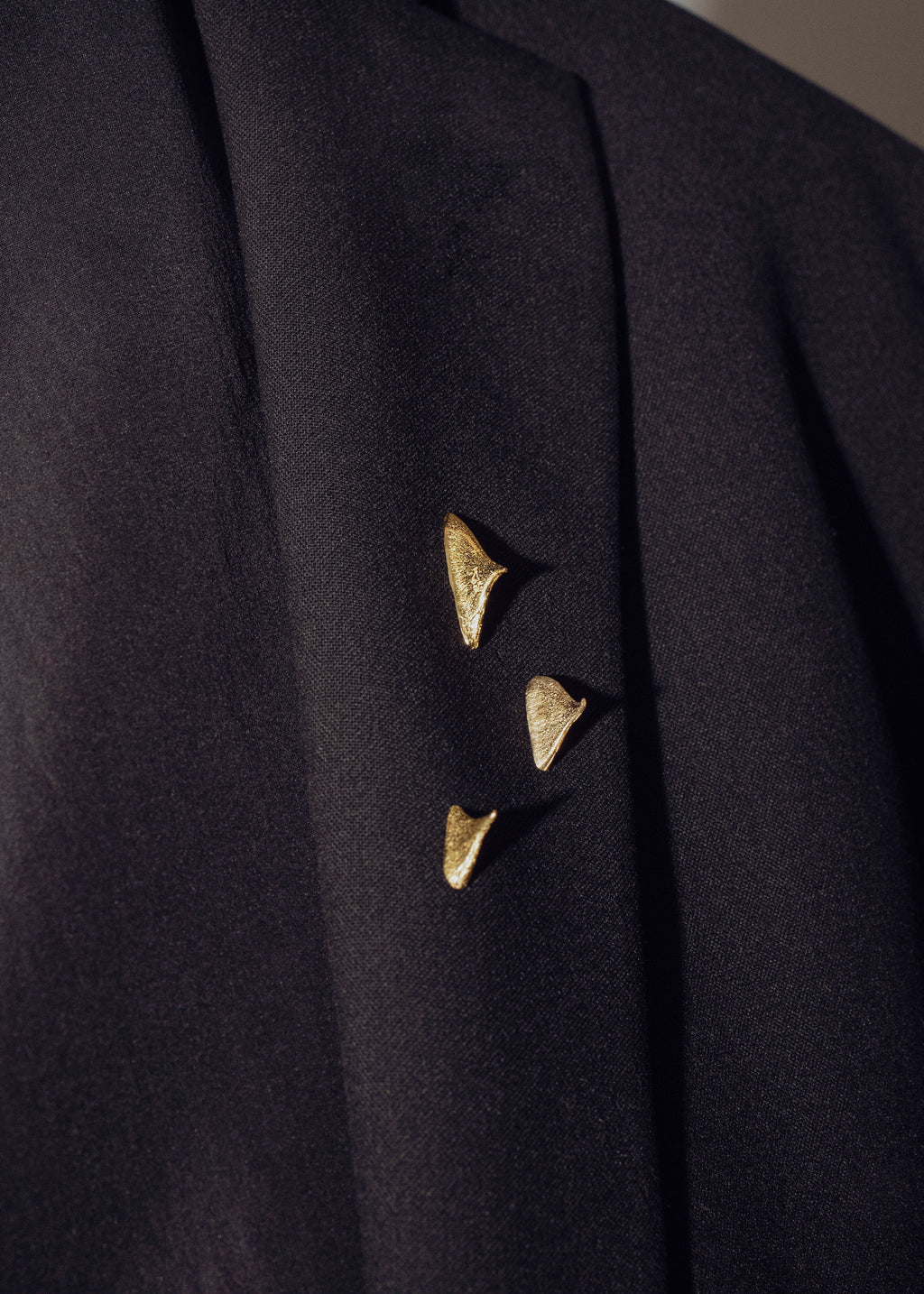 Close-up of a dark coat with handcrafted gold brooches on a neutral background
