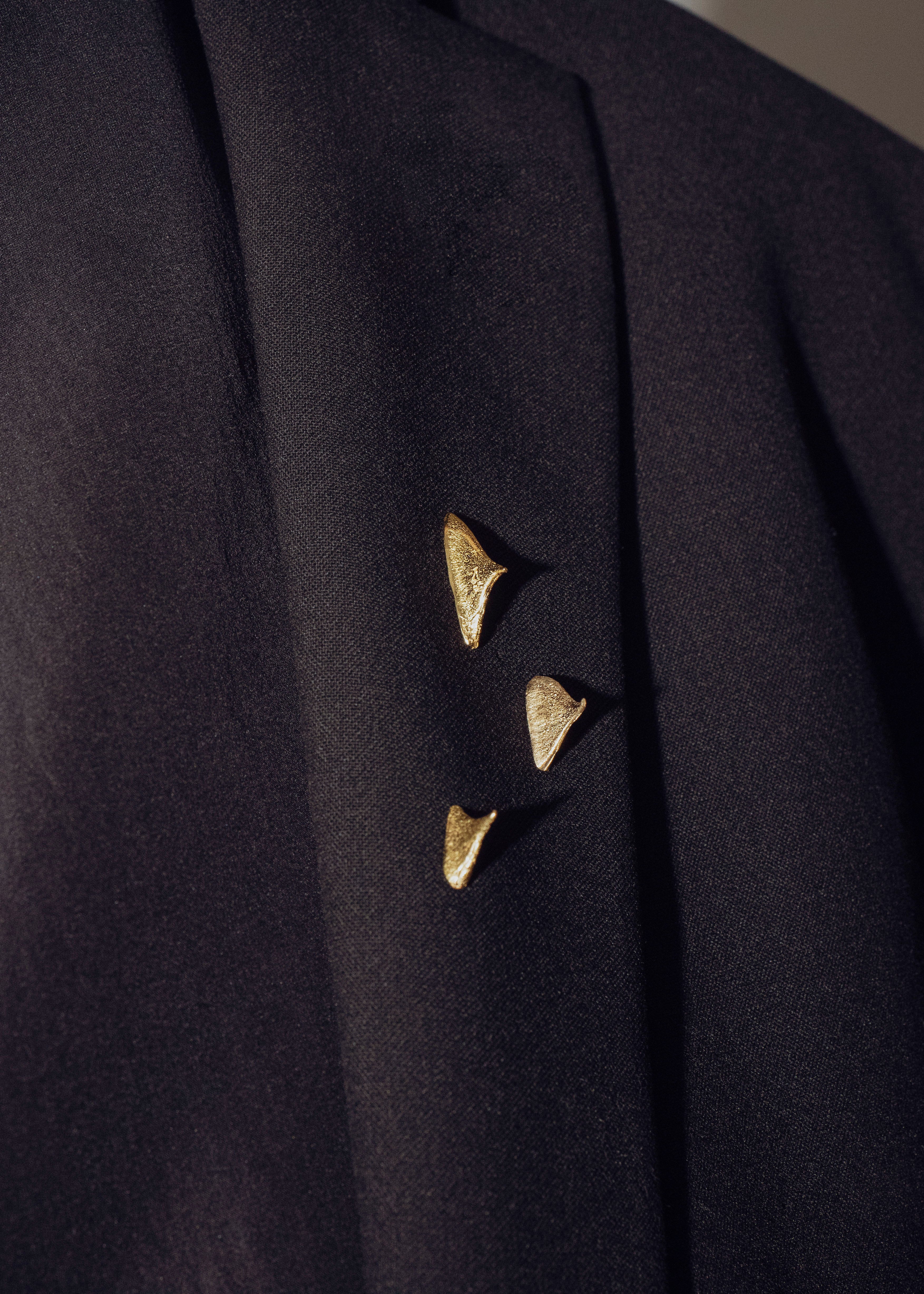 Close-up of a dark coat with handcrafted gold brooches on a neutral background