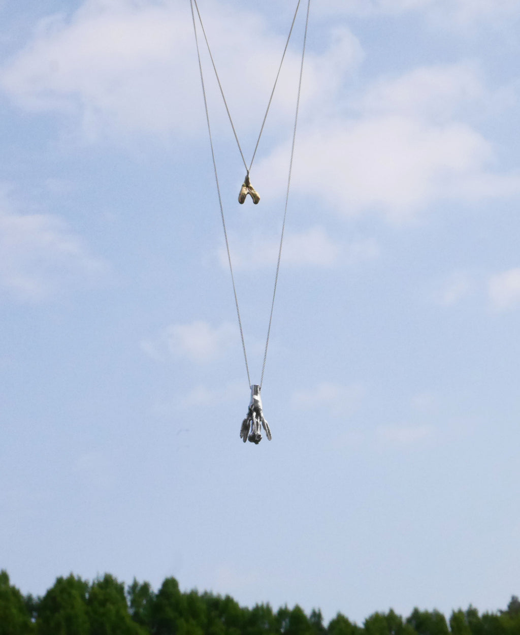 One gold handcrafted necklace and a silver handcrafted necklace with different pendants with the sky as background