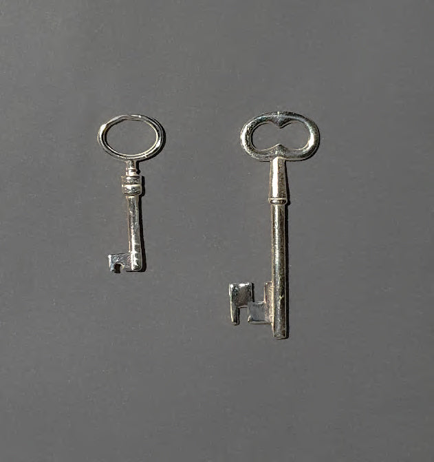 Two handcrafted silver keys on a dark gray background