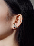Close-up of an ear wearing a handcrafted silver earring with a red gemstone, dark hair in the background