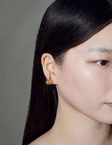 Close-up of a woman wearing a handcrafted gold earrings against a gray background