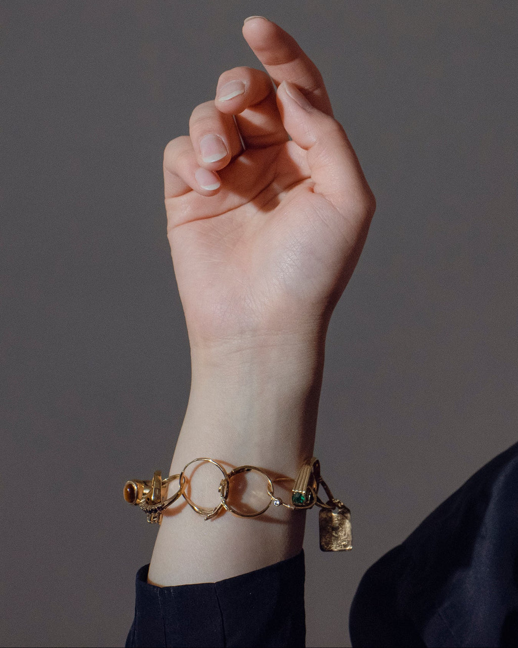 Hand wearing a handcrafted gold bracelet made out of rings against a neutral background