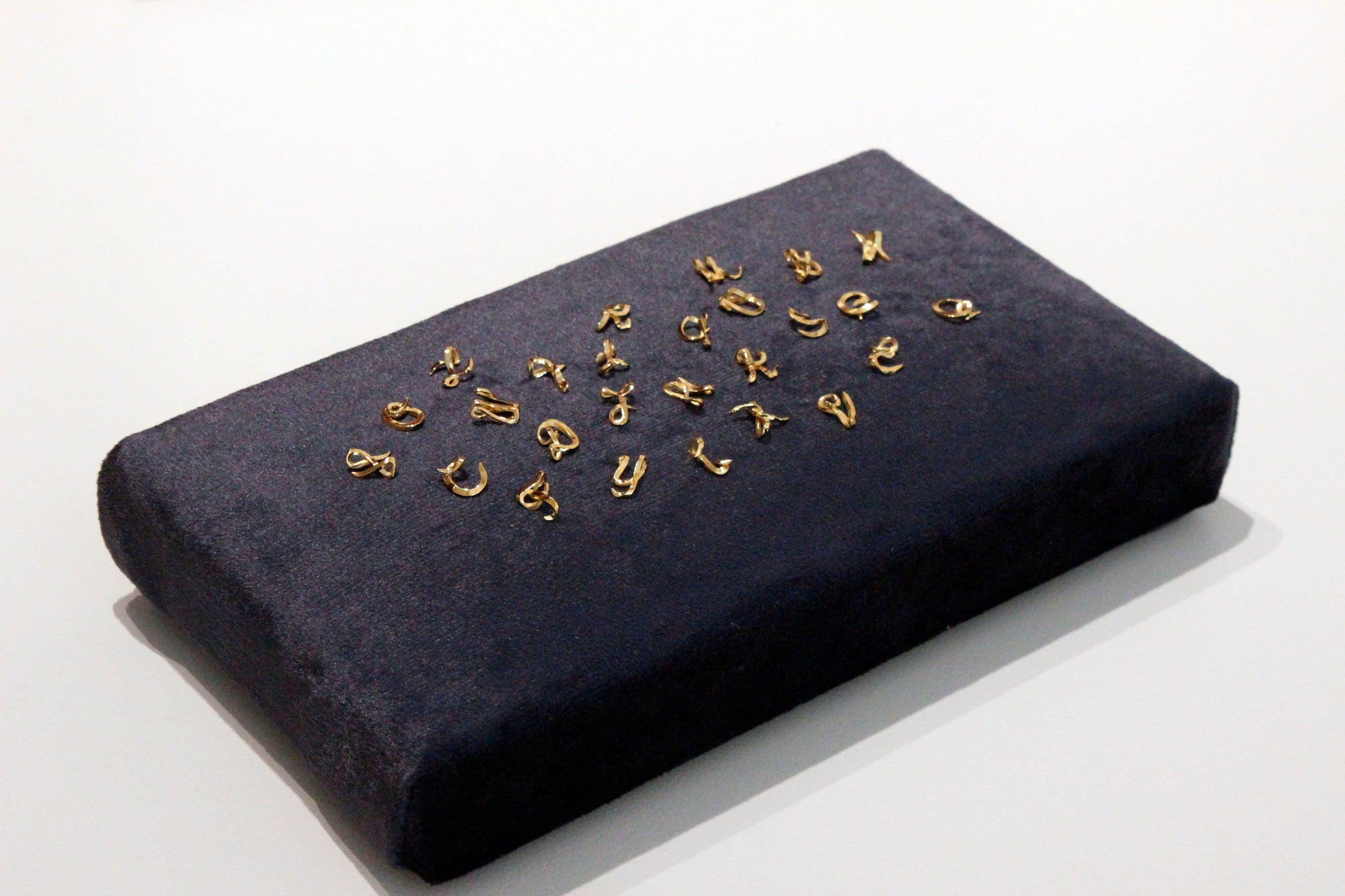 Blue velvet rectangular cushion with handcrafted gold initial charms on a white background
