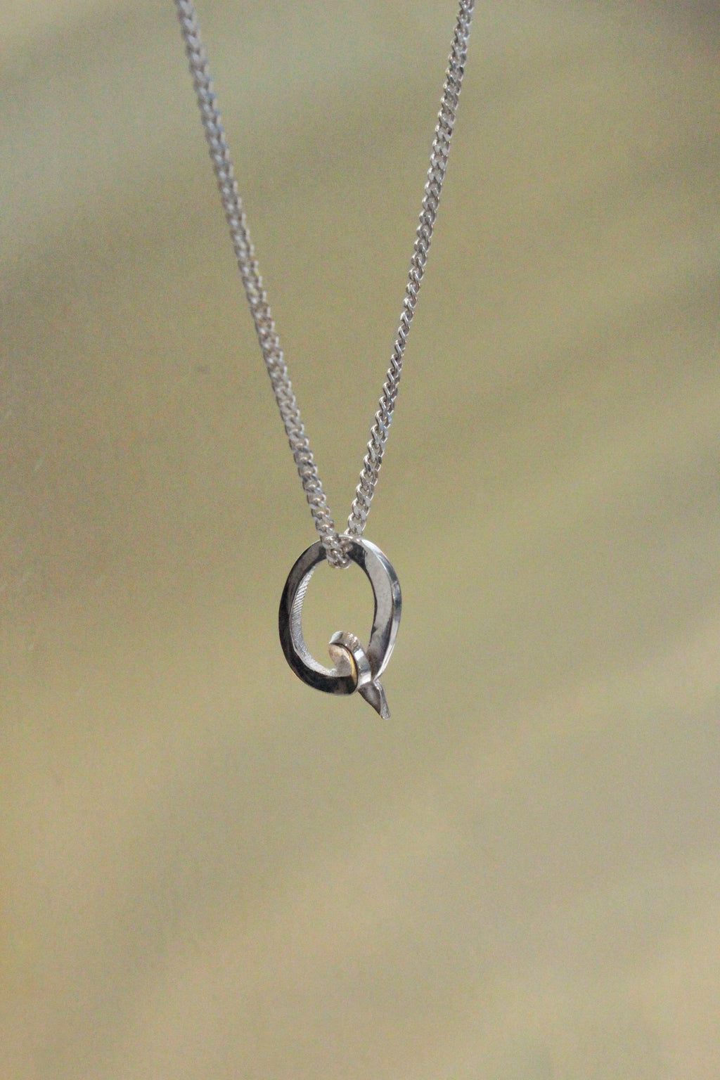 handcrafted Silver necklace with a Q letter pendant on a beige background