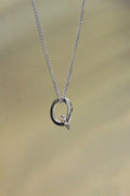 handcrafted Silver necklace with a Q letter pendant on a beige background