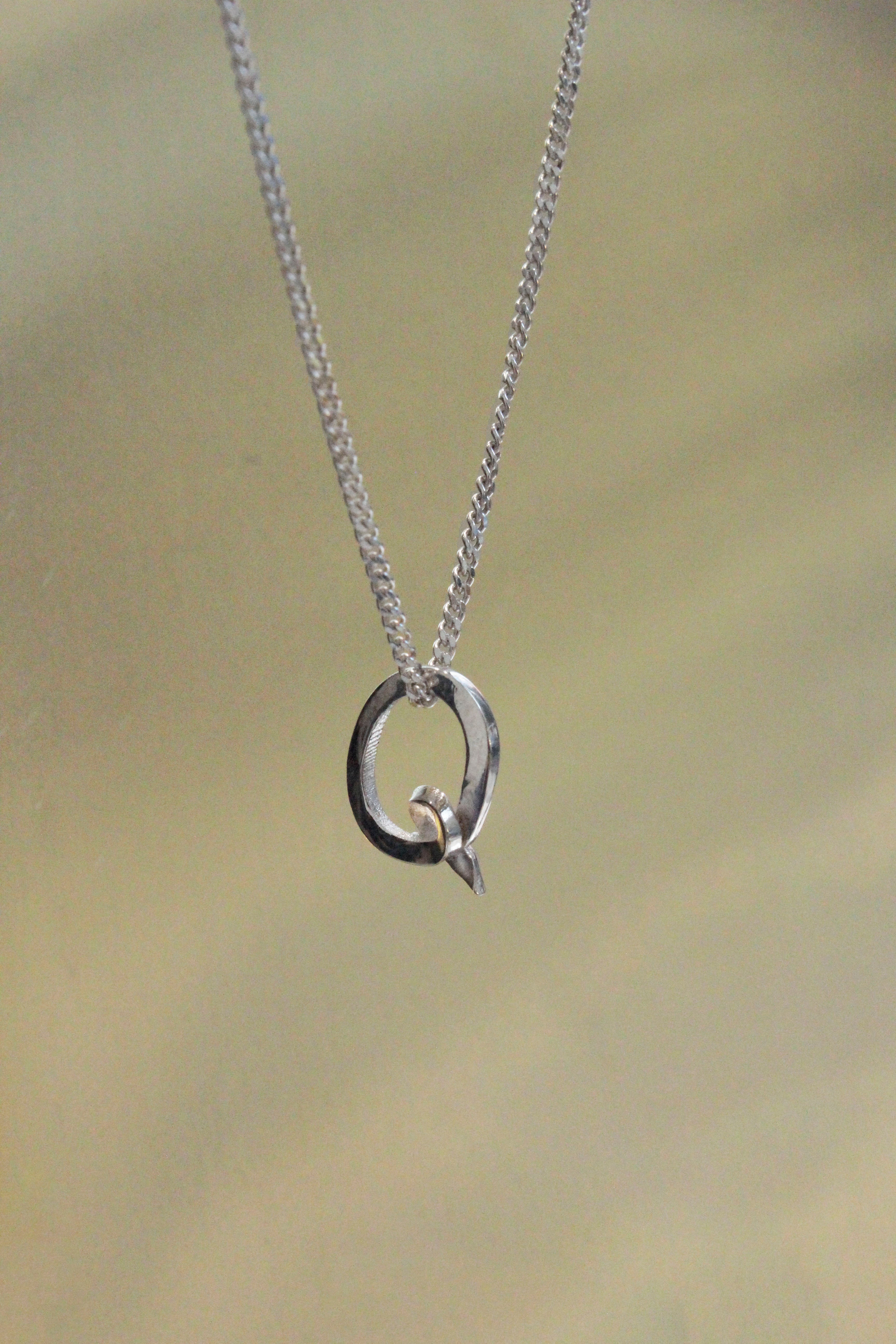 handcrafted Silver necklace with a Q letter pendant on a beige background