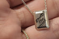 Silver pendant with engraved text held in a hand