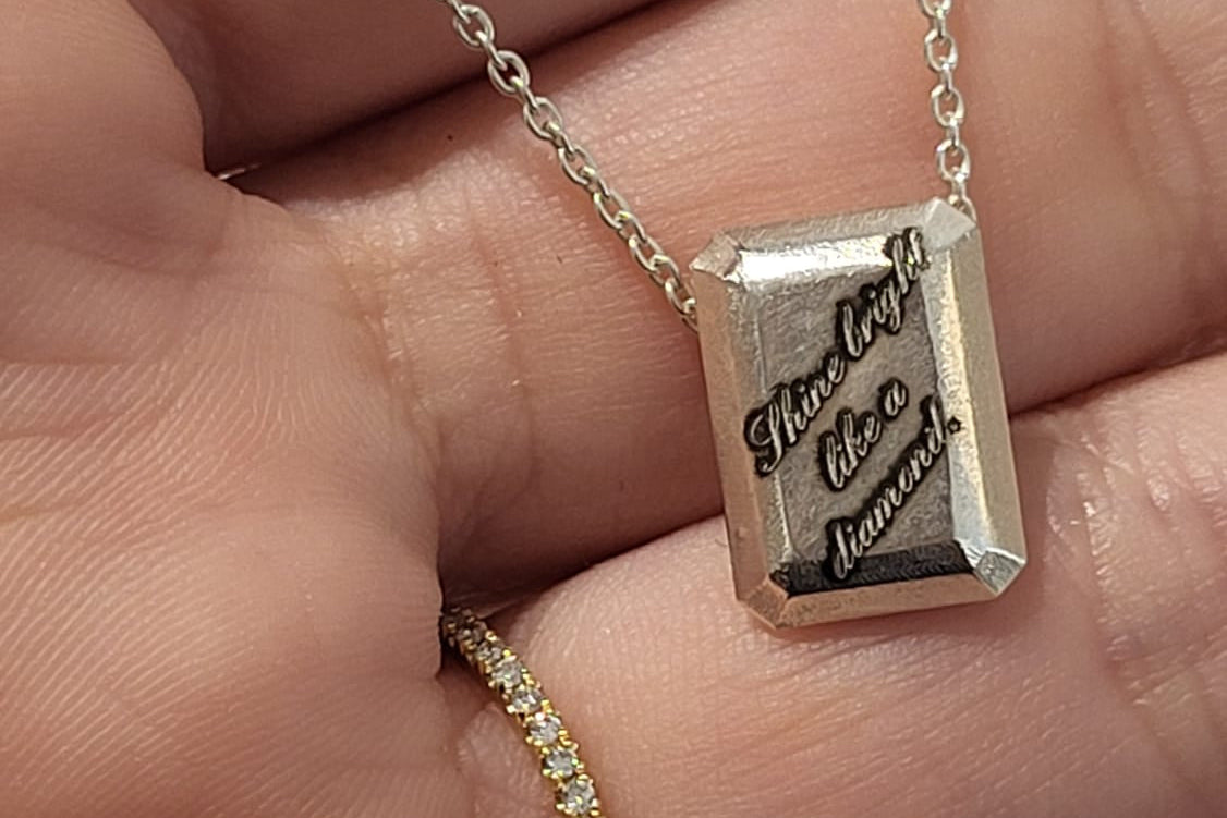 Silver pendant with engraved text held in a hand