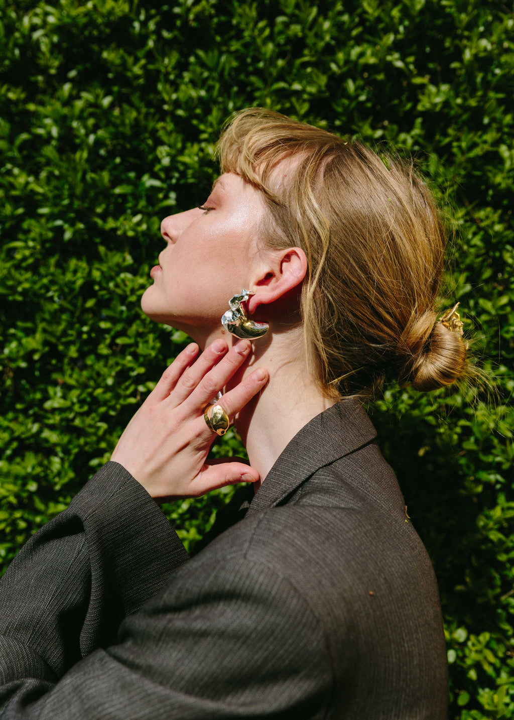Model adjusting her handcrafted silver orchid earrings against a green hedge background