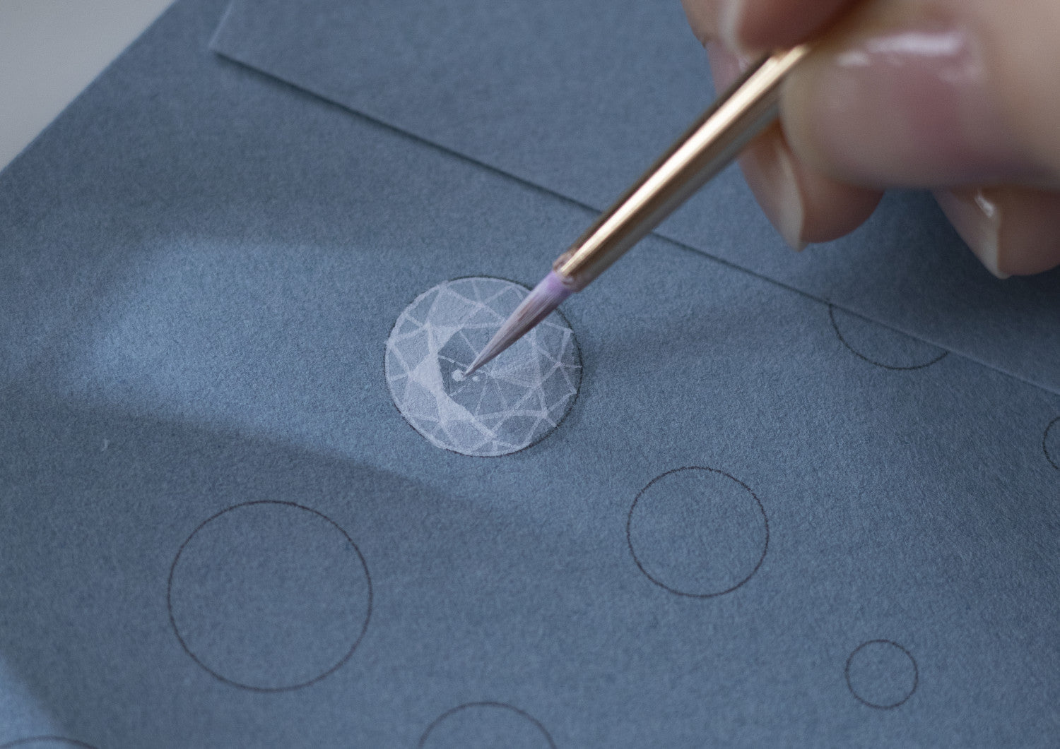 Hand using a small brush to apply a geometric design on blue paper