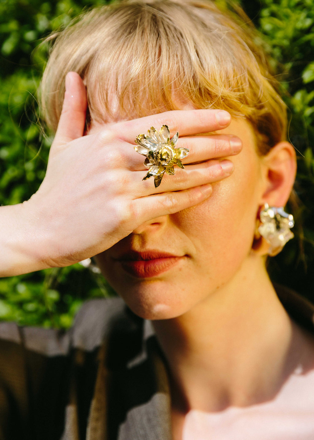 Model covering her eyes with a hand, wearing handcrafted Floret ring, against a blurred green background.