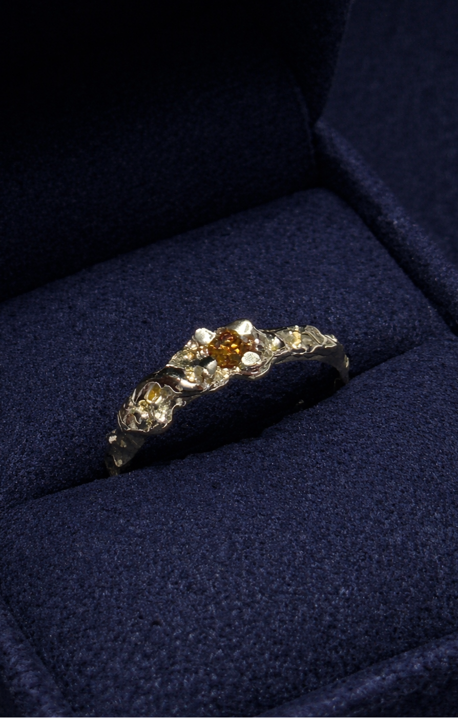 handcrafted gold ring with a central amber stone on a blue velvet cushion