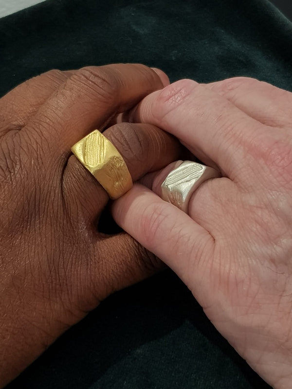Two hands wearing handcrafted gold and silver rings on a dark background