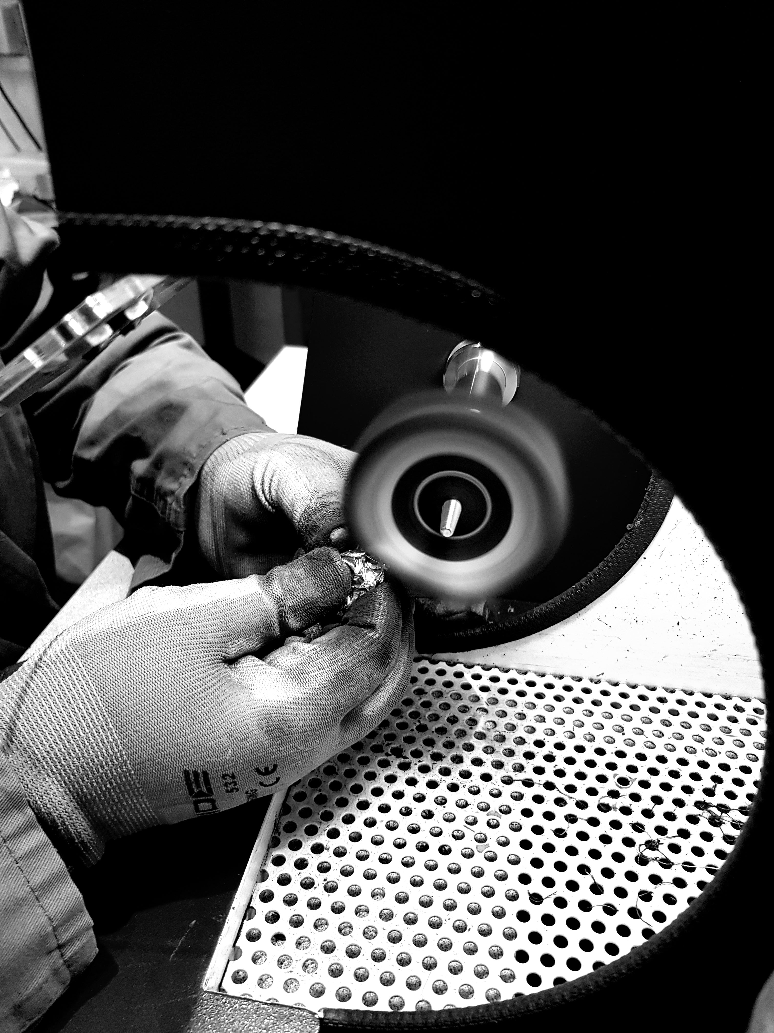 Person using a tool on a circular object with a textured surface, polishing jewelery