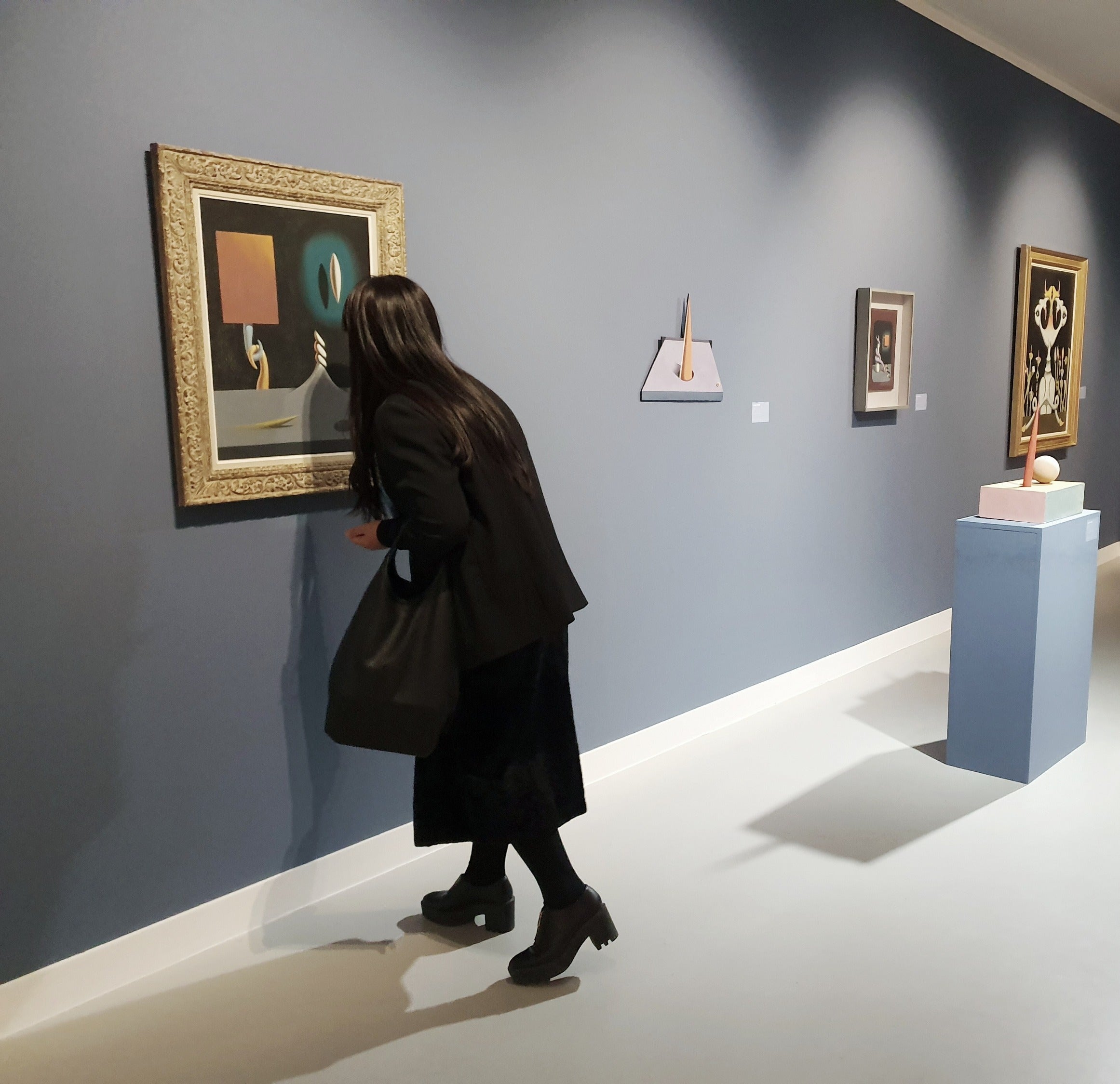 Person observing art pieces on a wall in an exhibition setting