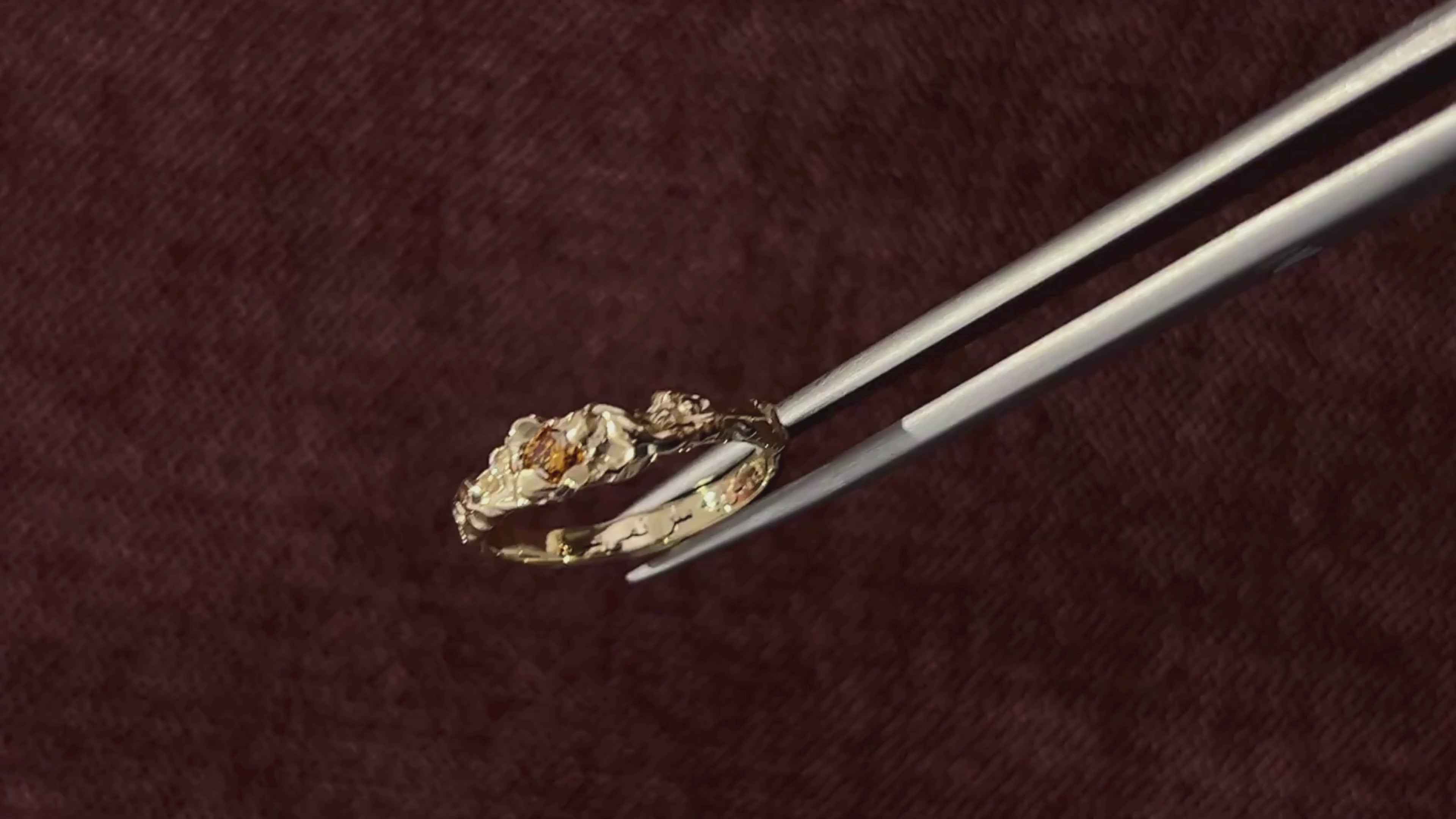gold custom engagement ring held up by tweezers in front of red velet background