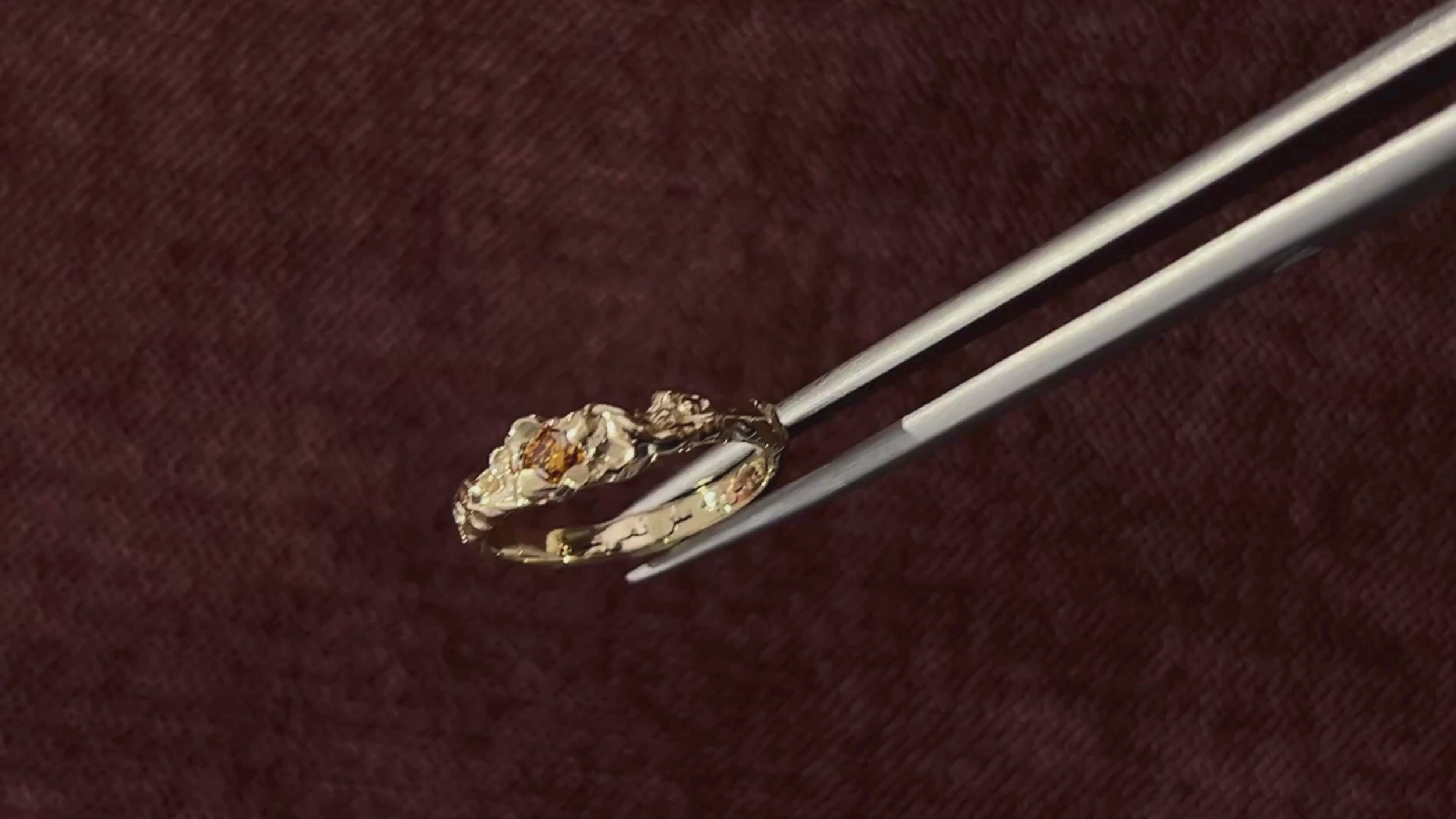 gold custom engagement ring held up by tweezers in front of red velet background